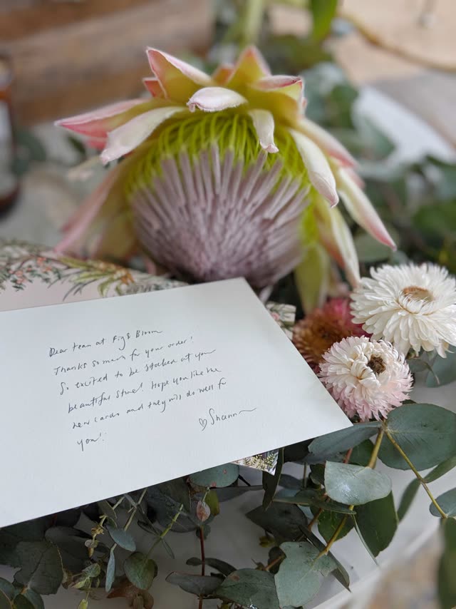 A handwritten thank-you note arranged beside a protea, dried flowers and eucalyptus leaves