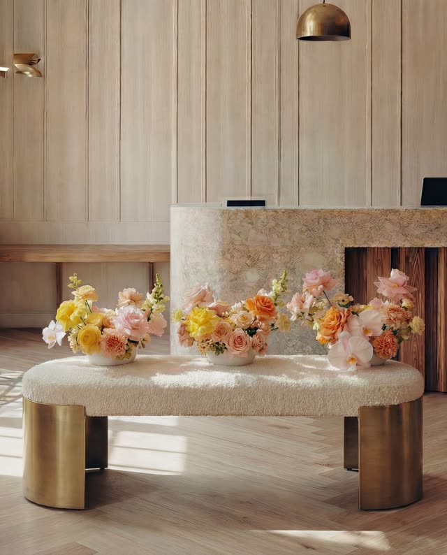 Three arrangements in soft pinks, yellows and oranges on a cream boucle bench in a warm, light-filled reception
