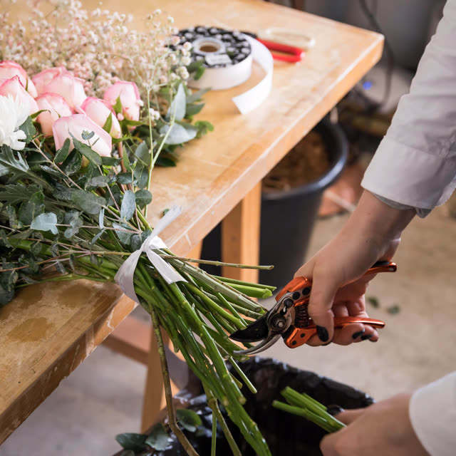Hands trimming fresh flower stems on a floristry workbench.